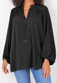 Blusa nera con un motivo testurizzato, presenta un colletto a V, maniche lunghe a sbuffo e un dettaglio con nodo al collo. Realizzata in tessuto leggero.