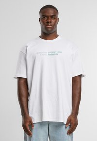 White cotton t-shirt with short sleeves, featuring blue text printed on the front: "Appreciate EVERYTHING Expect NOTHING." Simple design.