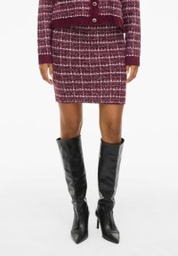 Burgunderrød strikket to-dels antrekk med rutete mønster; tettsittende skjørt og kort jakke kombinert med blanke svarte knelengde stiletthæler.