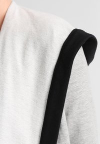 Tejido gris claro con una textura suave, que presenta un acento negro a lo largo del hombro. El diseño incluye un corte simple y moderno.