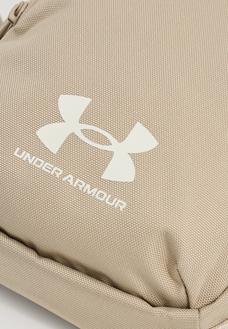 Pochette en tissu texturé beige arborant un logo Under Armour blanc. Le design présente des bords lisses et une forme robuste et structurée.