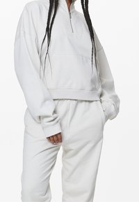 Felpa bianca con zip, colletto alto e tasca a marsupio, abbinata a pantaloni della tuta coordinati con polsini a costine e una vestibilità rilassata.