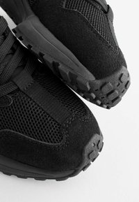 Czarne buty sportowe z siateczki i zamszu, wyposażone w teksturowaną gumową podeszwę oraz amortyzowaną konstrukcję dla zwiększonego komfortu.
