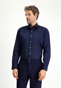 Granatowa koszula wizytowa z długim rękawem, kołnierzykiem na guziki, jednorzędowym zapięciem z przodu i błyszczącymi białymi guzikami, zestawiona z pasującymi ciemnymi spodniami.