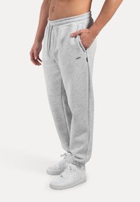 Szare bawełniane dresy z elastycznym pasem, bocznymi kieszeniami i ściągaczami przy mankietach, w połączeniu z białymi trampkami. Prosty, casualowy design.