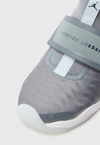 Γκρι αθλητικό παπούτσι με υφή στο πάνω μέρος, έντονο ιμάντα και λογότυπο, με γαλάζιες λεπτομέρειες και λευκή σόλα.