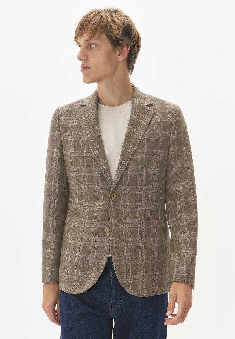 Brun rutigt kavaj i texturerad tyg, med två knappar och notch-krage. Kombinerad med en beige skjorta och blå jeans.