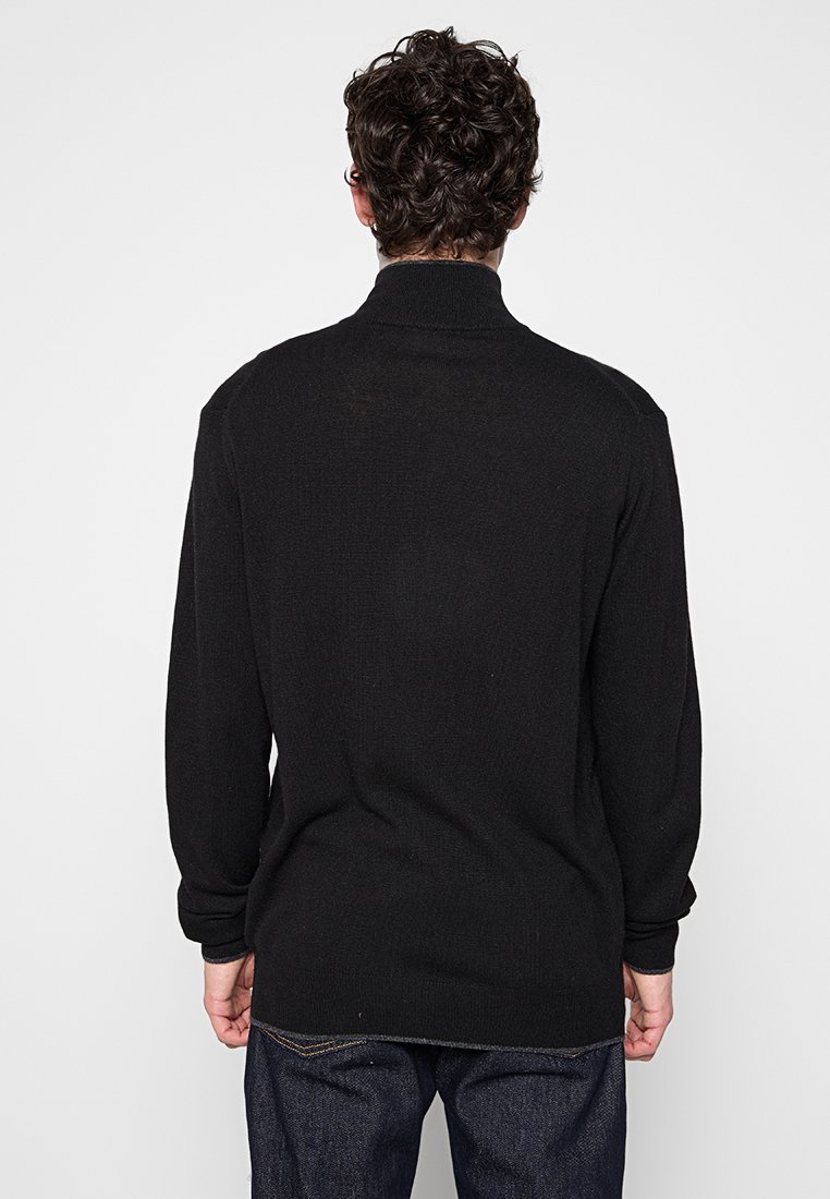 Suéter de punto negro con manga larga y cuello alto, con un acabado texturizado y sin patrones ni detalles de hardware visibles.