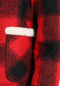 Rødt og sort ternet fleece-stof med et blødt hvidt foring, der fremhæver en lomme. Tekstureret udseende med et geometrisk mønster.