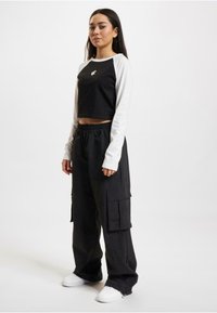 Black cropped long-sleeve top with white sleeves and logo, paired with black cargo pants featuring side pockets and white sneakers.