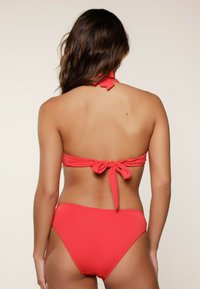Set di bikini rosso con top all'americana e chiusura a lacci, e pantaloni a vita alta coordinati. Tessuto liscio, senza motivi o dettagli.