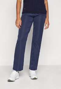 Navy blue trousers in a smooth, lightweight fabric with a straight-leg cut. Worn with white sneakers and a textured navy top.