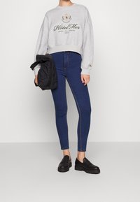 Sweatshirt gris court avec le texte "Hotel Mer" en vert foncé, associé à un jean bleu foncé ajusté et des chaussures noires à plateforme sans lacets.
