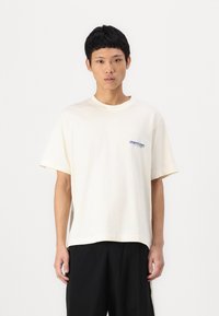 Cremefarvet bomulds T-shirt med korte ærmer, med et blåt broderet logo på venstre bryst og en afslappet pasform.