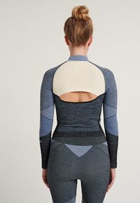 Top deportivo en varios tonos de azul con detalles texturizados. Presenta un corte en la parte de atrás y un diseño ajustado con mangas largas.