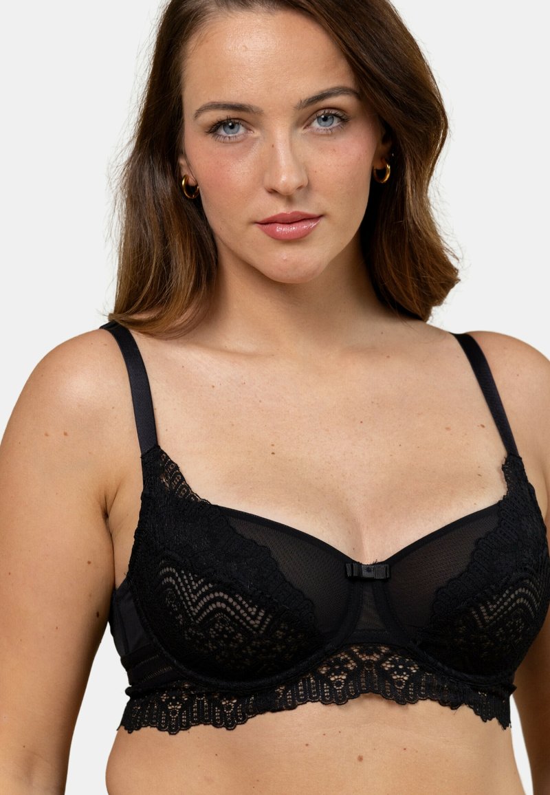 Soutien-gorge en dentelle noire avec panneaux en mesh, armatures, bords festonnés et bretelles réglables. Petit nœud minimaliste au centre.