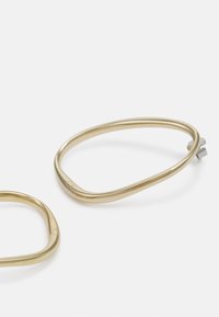 Aros de metal en tono dorado con un diseño suave y redondeado y una forma minimalista; cuenta con un pequeño acento plateado para el cierre.