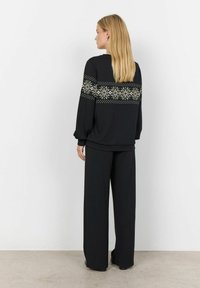 Zwarte trui met lange mouwen, voorzien van een geperst decoratief band in roomkleur over de rug. Gecombineerd met zwarte wijde broek.