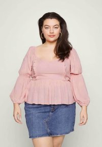 Top peplum em rosa blush com mangas bufantes, apresentando detalhes de babados e um acabamento texturizado, combinado com uma saia mini de ganga.