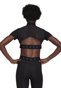 Černý sportovní crop top s vysokým límcem a výřezem na zádech. Nosit s odpovídajícími černými legínami, které mají elastický pas a logo.