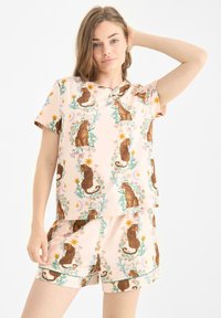 Svetle růžové pyžamo s opakujícím se vzorem leopardů a květinových motivů. Krátký rukáv a šortky s kontrastními detaily.