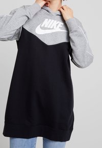 Sudadera con capucha Nike tipo pulóver que presenta una parte superior gris con una sección inferior negra, un gran logo blanco y tela suave con un ajuste holgado.