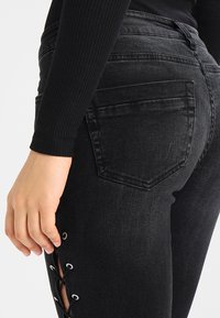 Črne skinny jeans hlače z čipkastimi detajli na straneh, ki imajo pet žepov in rahlo zbledel videz, zasnovane za oprijet silhueto.