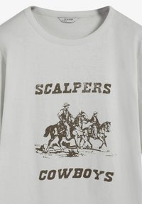 Camiseta de algodón gris claro con un estampado gráfico marrón de vaqueros a caballo y el texto "SCALPERS COWBOYS" debajo. Cuello redondo.