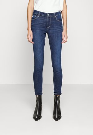 Slim-fit mørkeblå jeans båret med en hvid top og sorte ankelstøvler med spids snude og lynlåse foran.