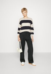 Pull rayé en crème et marine, doté de manches longues et d'une coupe décontractée. Associé à un pantalon noir taille haute et des baskets blanches.