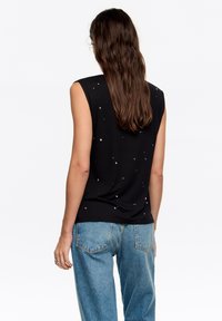 Czarna, bezrękawnikowa bluzka o luźnym kroju, ozdobiona rozproszonymi, srebrnymi aplikacjami, zestawiona z jasnoniebieskimi, wysokim stanem dżinsami.