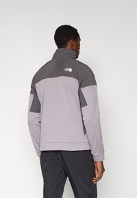 Gray long-sleeve jacket with a high collar, featuring dark gray panels, ribbed texture, and an embroidered logo at the back.