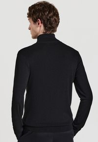 Maglione a collo alto nero realizzato in tessuto a maglia, con maniche lunghe, vestibilità slim e orli e polsini a coste, mostrato di schiena.