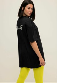 T-shirt nera oversize con maniche corte e testo sul retro. Abbinata a leggings gialli brillanti. Tessuto morbido, design casual.