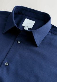 Sötétkék, slim fit ing texturált anyagból, gombos elejű és klasszikus gallérral. A méretet és a márkát tartalmazó címke található rajta.