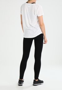 Camiseta blanca, ligera y de manga corta, con dobladillo redondeado, combinada con leggins negros ajustados y zapatillas deportivas negras. Diseño simple y casual.
