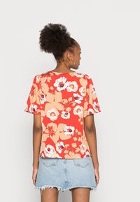 Blusa curta de manga curta vermelha com um corte descontraído, apresentando grandes flores em tons de creme e pêssego, usada com uma saia de ganga azul clara.