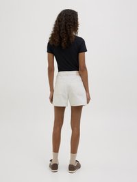 Λευκές βαμβακερές σορτς με πίσω τσέπες, σε συνδυασμό με μαύρο μπλουζάκι και καφέ αθλητικά παπούτσια, εμφανισμένα από πίσω με ουδέτερο φόντο.