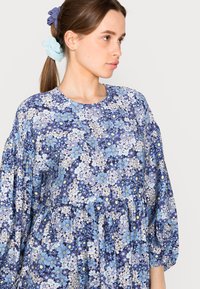 Vestido estampado floral em tons de azul com decote redondo e mangas bufantes. Tecido suave com uma cintura franzida e padrões de flores variados.