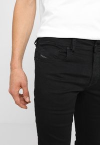 Svart denim jeans med slim fit, med en framlomma och subtila sömnadsdetaljer, i kombination med en vit skjorta.