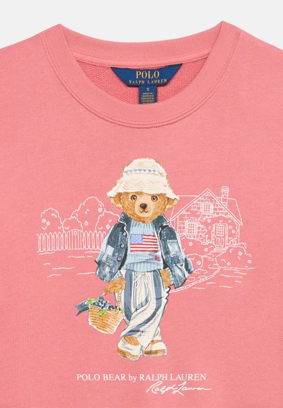 Ροζ πουκάμισο με αρκούδα που φοράει κουβά καπέλο, τζιν μπουφάν, ριγέ παντελόνια, κρατώντας καλάθι, με περίγραμμα σπιτιού και φράχτη στο φόντο.