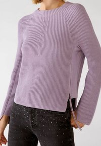 Lilac knitted sweater with a ribbed texture, round neckline, and side zipper detail. Paired with dark jeans featuring studded accents.