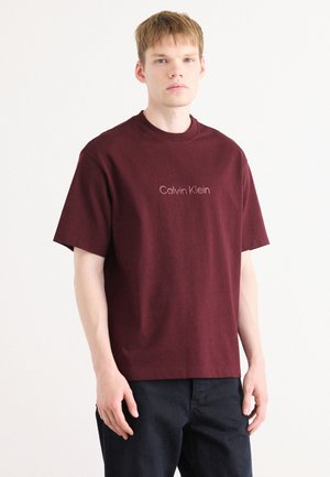 Maroon cotton t-shirt with a crew neck and short sleeves, featuring the "Calvin Klein" logo in subtle beige lettering on the front.