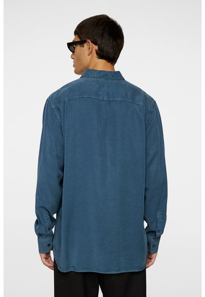 Langärmliges, knöpfbares Hemd aus einem verblassten blauen Stoff mit einer glatten Textur. Verfügt über einen Kragen, geknöpfte Manschetten und einen lockeren Schnitt.