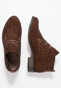 Stivaletti in suede marrone con motivo leopardato, punta tonda, design con lacci e tacco basso impilato nero. Gli accenti includono dettagli di cucitura.