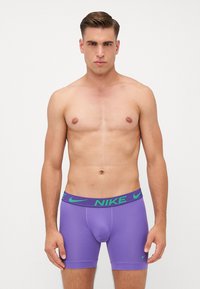 Lilla Nike boxer briefs med en grøn stribet talje, der har Nike-logoet. Glat, strækbart stof og midt-til-lår længde.