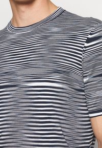 Primer plano de una persona que lleva una camiseta de rayas azul marino y blanca, con un cuello redondo, mostrando la textura de la tela y el patrón de rayas.