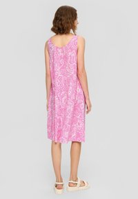 Rosa ärmelloses Kleid mit weißen Blumenmustern, knielang, aus weichem Stoff und mit tiefem Rückenausschnitt, kombiniert mit weißen Riemchensandalen.