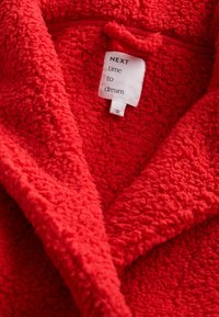 Roter Fleece-Bademantel mit weicher, strukturierter Oberfläche und Schalkragen; ausgestattet mit einem Pflegeetikett, auf dem steht: "Nächste Gelegenheit zum Träumen."
