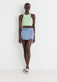 Top corto verde a coste, mini gonna in denim blu chiaro con chiusura a bottoni e sandali a scivolo argentati. Design semplice con un look informale.